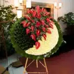 Round funeral wreath on wooden stand with red anthuriums, white flowers, and dark green leaves arranged in a yin yang style