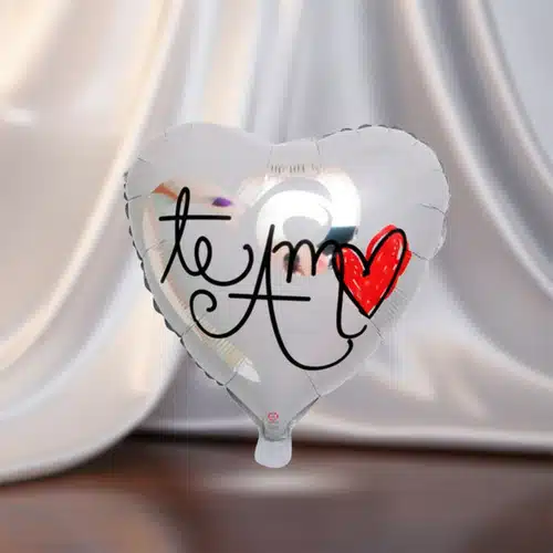 Globo plateado en forma de corazón con la frase te amo y un corazón rojo dibujado, sobre fondo de tela blanca difuminada