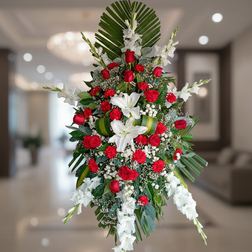 Arreglo floral fúnebre en forma ovalada con rosas rojas, lirios blancos y follaje verde sobre fondo de interior elegante desenfocado