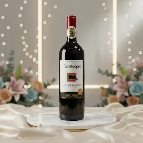 Botella de vino tinto GatoNegro Cabernet Sauvignon San Pedro sobre una base redonda de mármol blanco, con fondo desenfocado de luces cálidas y arreglos florales