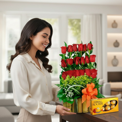 Mujer joven de cabello oscuro mirando un arreglo floral de rosas rojas en varios niveles con follaje verde, colocado sobre una mesa junto a una caja de chocolates Ferrero Rocher