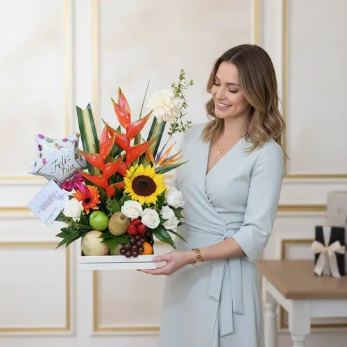 Mujer joven con vestido celeste claro sosteniendo una bandeja blanca con arreglo de flores tropicales, girasol, rosas blancas, frutas variadas y un globo que dice Feliz Día en un interior elegante