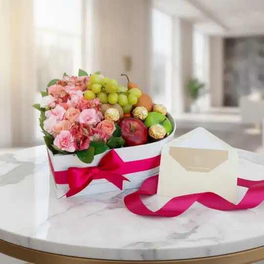 Arreglo floral AMOS en caja corazón con rosas, alstroemerias, frutas frescas y chocolates Ferrero Rocher, sobre mesa de mármo