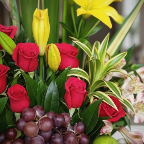 Primer plano extremo de Arreglo Floral con Frutas Akebia, destacando rosas rojas, lirios amarillos, uvas y hojas verdes con g