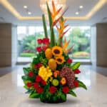 Arreglo floral premium con rosas rojas, girasoles, aves del paraíso, frutas durio, uvas y manzanas, sobre mármol en un lobby