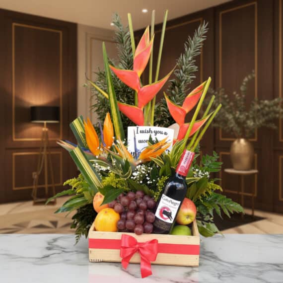 Arreglo Floral con Frutas Platonia y Vino Tinto para Regalar Arreglo floral Platonia con heliconias, aves del paraíso, uvas, manzanas, duraznos y botella de vino tinto, sobre mármol en u