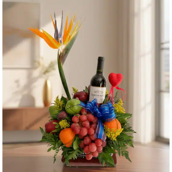 Arreglo Floral Gourmet ITALINA: Vino y Frutas Exóticas para Regalar Arreglo floral gourmet ITALINA con ave del paraíso, vino tinto, uvas, manzanas, naranjas y ciruelas, sobre una mesa de madera