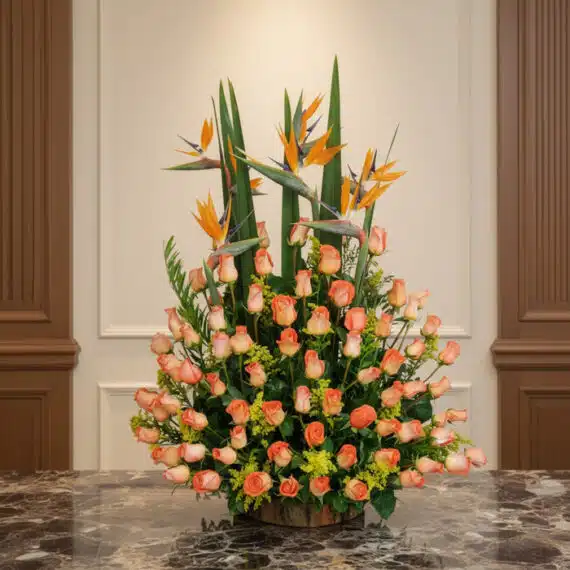 Arreglo floral grande con rosas color salmón y aves del paraíso, sobre una mesa de mármol en un entorno elegante de hotel bou