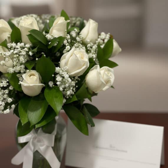 Fotografía macro premium del Arreglo Fúnebre Pétalos del Alma con rosas blancas, follaje verde, rocío sutil y cinta satinada.