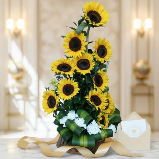 Arreglo floral alto con girasoles amarillos vibrantes y flores blancas, base de madera, cinta dorada, sobre elegante, sobre s