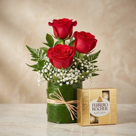 Arreglo Floral de Rosas Rojas y Bombones Ferrero Rocher Elegante arreglo floral con tres rosas rojas vibrantes, follaje verde y flores blancas, acompañado de una caja de bombones Fe