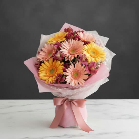 Bouquet de gerberas multicolor en tonos pastel (rosas y amarillas) con alstroemerias, envuelto en papel rosa y blanco, sobre