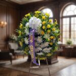 Corona fúnebre 'Estamos Contigo' con flores amarillas y blancas, lazo morado, en sala de velación premium con luz natural sua
