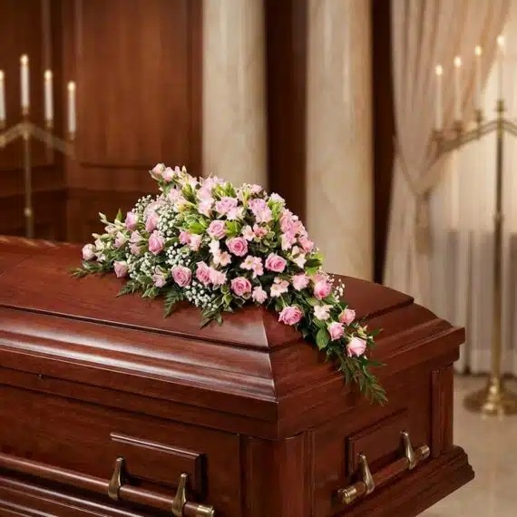 Cubre Caja Fúnebre en Homenaje a Juana con Rosas Rosadas Cubre caja fúnebre elegante con rosas rosadas y follaje verde, delicadamente dispuesto sobre un ataúd de madera oscura en un