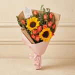 Ramo Beatrice con rosas salmón, girasoles vibrantes y eucalipto, envuelto en papel kraft y rosa, ideal para regalar en cualqu